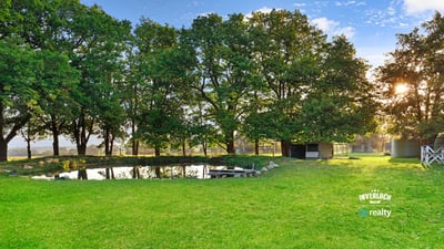 Expansive green space features a tranquil pond, surrounded by mature trees, perfect for outdoor gatherings.