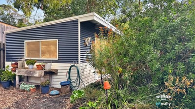 Quaint cottage nestled among lush greenery, offering a unique retreat with potential for creative landscaping.