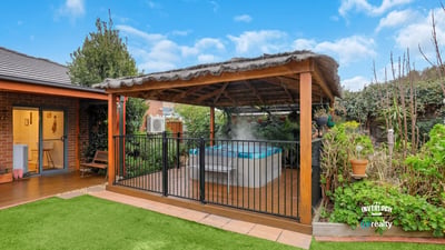 Discover a relaxing outdoor oasis featuring a covered patio and inviting hot tub surrounded by lush greenery.