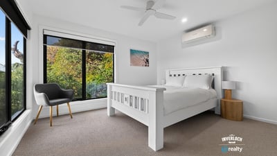 Bright bedroom with large windows showcasing natural light and leafy views, featuring modern finishes and comfort.