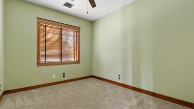 Featuring green walls, soft carpeting, and a ceiling fan, this secondary bedroom offers comfort and charm in a tranquil corner of the house.