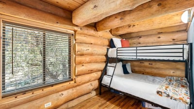 Cozy bunk room with log walls and hardwood floors, offering flexible sleeping arrangements while preserving the cabin-style aesthetic.
