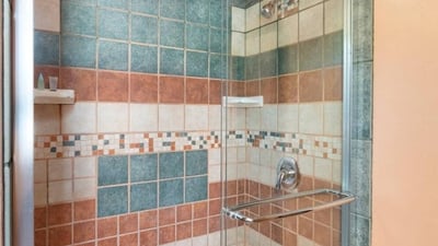 Bathroom shower featuring decorative tilework and glass doors, providing durability and easy maintenance within a rustic setting.