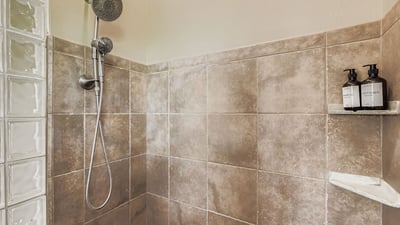 Primary bathroom showcases a tiled walk-in shower with multiple shower heads and sleek fixtures for added comfort.