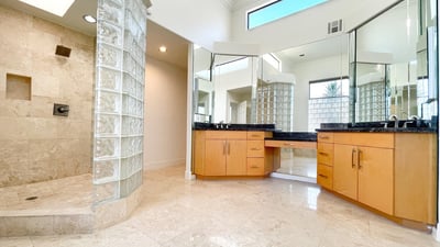 Light-filled primary bath with matching granite vanities, makeup station, and a custom glass shower enclosure for a luxurious touch.