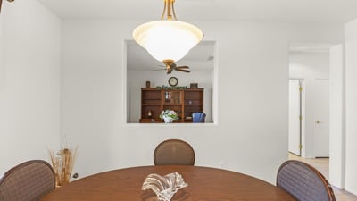 A modern dining area framed by crisp white walls and elegant lighting, offering a clear view into the private home office beyond.