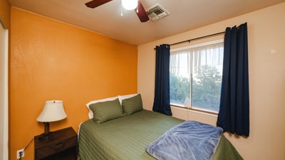 A cozy bedroom space offering soft lighting, ceiling fan, and window views of the natural desert surroundings. Ideal for guests or flexible use in this tranquil Hackberry home.