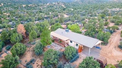 This elevated view highlights the wraparound deck, mature trees, and sprawling land. A serene retreat with endless possibilities for customization or self-sufficient living.