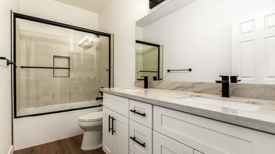 Updated Scottsdale guest bathroom with dual sinks, contemporary cabinetry, and modern black fixtures. The bathroom also includes a glass shower enclosure and elegant finishes that complement the home s remodeled interior.