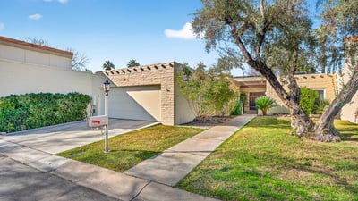 Clean, well-kept front exterior with attached garage, private walk-up entry, and manicured landscaping inside a secure Phoenix community.
