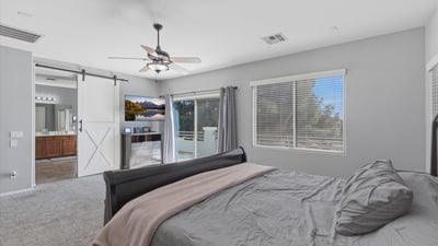 Spacious primary bedroom with plush carpet, ceiling fan, and neutral tones, offering a relaxing retreat within this well-designed Queen Creek home.
