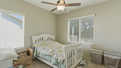 Comfortable secondary bedroom with plush carpet, ceiling fan, and large windows that bring in natural light, creating a welcoming space for guests or family.