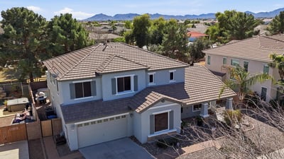 Elevated drone view showing the home's position within the neighborhood with distant mountain scenery and surrounding residential streets in Queen Creek.