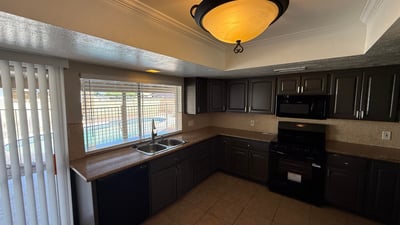Well-designed kitchen featuring dark cabinets, tile flooring, and practical layout. The sink window overlooks the fenced backyard and pool, bringing outdoor views into the space.