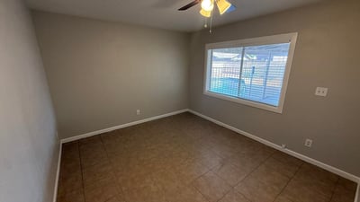 Guest bedroom with tile flooring, neutral colors, and ceiling fan for comfort. Large window allows natural light while maintaining a calm and inviting atmosphere.