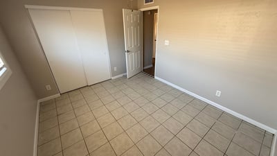 Bedroom with sliding closet doors, tile flooring, and ceiling fan lighting. Neutral finishes provide a clean and versatile interior space.