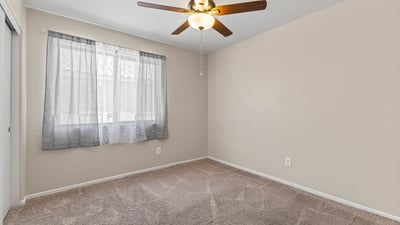 Comfortable bedroom with soft carpeting, ceiling fan, and closet space ideal for guests or family members.