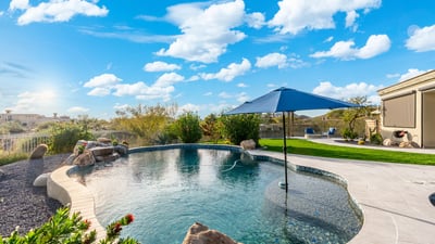 Scottsdale pool featuring built-in umbrella seating area, surrounded by pavers and landscaped yard, ideal for outdoor enjoyment.