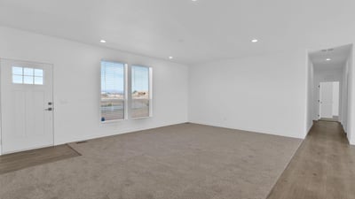 Welcoming front living room featuring soft carpeting, recessed lighting, and oversized windows. The spacious layout offers flexibility for entertaining guests, family activities, or creating a relaxing everyday living environment.