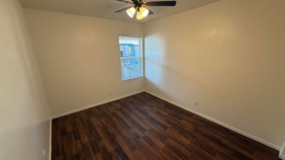 Comfortable bedroom featuring wood-look flooring, ceiling fan, and natural light. The spacious layout provides a relaxing retreat while accommodating a variety of furniture configurations.