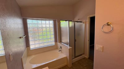 Primary bathroom designed for relaxation with a garden tub, separate shower, tile flooring, and large window. The bright and functional layout adds comfort and value to this Goodyear home.
