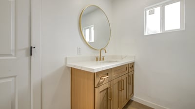 This remodeled bathroom highlights a quartz countertop, custom wood vanity, designer gold faucet, round mirror, and contemporary finishes for a polished modern look.