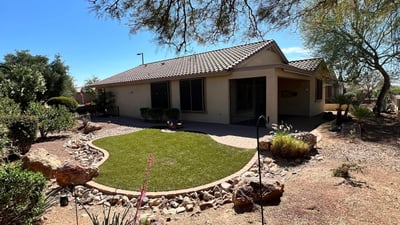 Beautiful backyard showcasing lush artificial turf, paver pathways, decorative rock features, mature desert plants, and tranquil golf course surroundings. A perfect outdoor retreat for relaxing or entertaining guests.