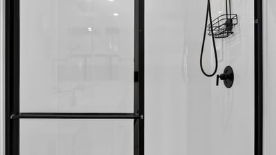 The oversized walk-in shower features sleek glass doors, contemporary black fixtures, built-in storage shelves, and a low-maintenance design that enhances the spa-like feel of the primary bath.