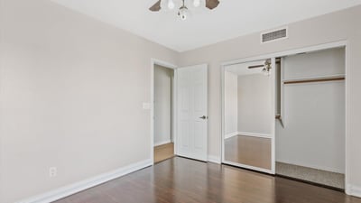 Featuring rich wood flooring, mirrored closet doors, and a ceiling fan, this spacious bedroom provides comfort, storage, and flexibility for guests or family members.