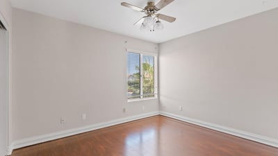 Large windows bring abundant natural light into this inviting bedroom featuring wood flooring, neutral finishes, and a ceiling fan. A comfortable space that complements this Chandler home.