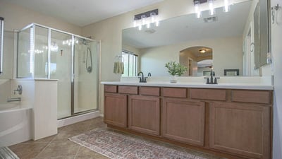 Elegant primary bathroom with an extended dual-sink vanity, oversized mirror, updated lighting, soaking tub, and separate glass shower. A spacious and functional owner's retreat.