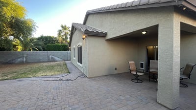 Backyard view featuring an extended paver patio, covered seating area, and lawn space that offers flexibility for outdoor entertaining and everyday enjoyment.