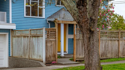 This inviting home features a unique yellow door, framed by a well-maintained wooden fence and inviting landscaping.