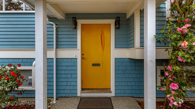 Bright yellow door welcomes you to this inviting home, framed by lush greenery and vibrant blooms.