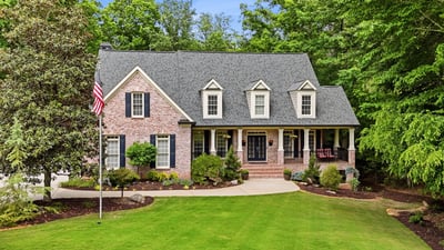 This beautiful home features a welcoming front porch, expansive lawn, and lush surrounding greenery for privacy.