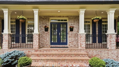 Welcoming entrance features a brick facade, dual blue doors, and attractive landscaping for a polished look.