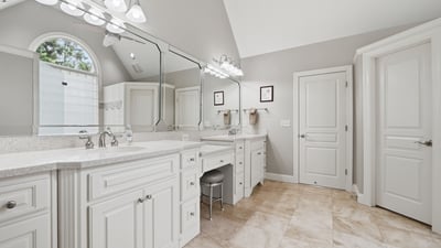 Spacious bathroom featuring dual vanities, modern fixtures, and abundant natural light from an arched window.