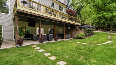 Spacious outdoor living area features a deck overlooking a lush, landscaped yard with stone pathways.
