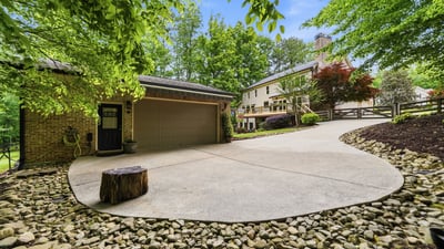 Spacious driveway with natural landscaping offers a welcoming approach to this unique property surrounded by trees.