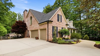 Stunning brick home with a spacious driveway, surrounded by lush landscaping and mature trees.