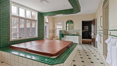 Spacious bathroom featuring a large sunken tub, extensive green tilework, and ample natural light.
