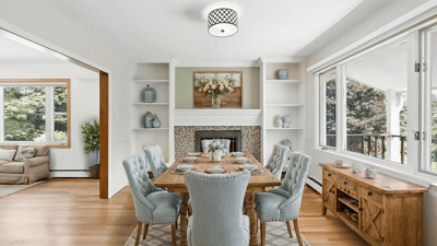 Bright dining area featuring built-in shelves, a cozy fireplace, and large windows overlooking a lush landscape.