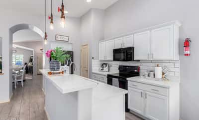 Featuring quartz countertops, subway tile backsplash, white cabinetry, pendant lighting, and generous prep space, this bright kitchen blends timeless style with everyday functionality.