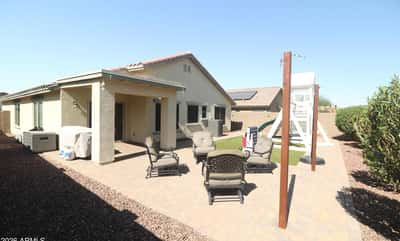 A covered patio overlooks the spacious backyard featuring paver hardscaping, low-maintenance landscaping, and artificial turf. Designed for comfortable outdoor enjoyment throughout the year.