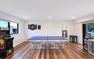 Bright recreational space featuring a ping pong table, arcade machine, and dartboard for entertainment.