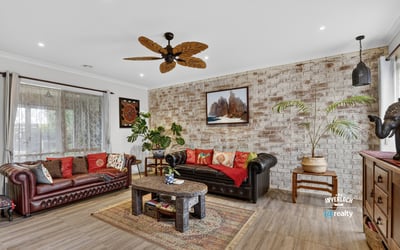 Spacious living area featuring a unique brick wall, rich colors, and a tropical-inspired ceiling fan.