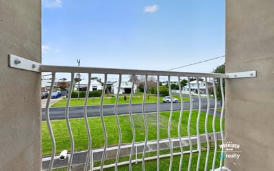 Enjoy a peaceful balcony view overlooking a quiet street surrounded by greenery and residential homes.