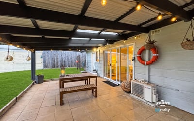 Spacious outdoor patio with hanging lights and lawn, perfect for gatherings and relaxed evenings.
