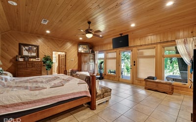 Spacious master bedroom featuring wood accents, large windows, and direct access to outdoor greenery.