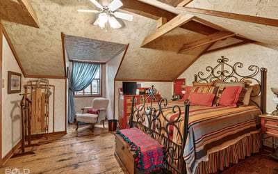 Cozy loft bedroom featuring exposed beams, a unique design, and ample natural light from large windows.